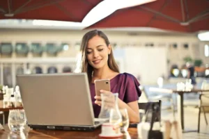 Una ragazza col telefono sui social al tavolo di un bar di giorno | PostPickr