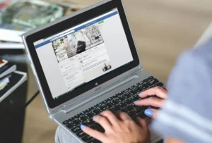Pagina Facebook aziendale visualizzata su un laptop in grembo a una donna con le unghie laccate | PostPickr
